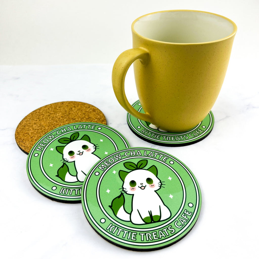 Cute green coasters featuring a white cat with green tipped ears, feet, and tail with the text "Meow cha latte" and "Kittie Treats Cafe" around it