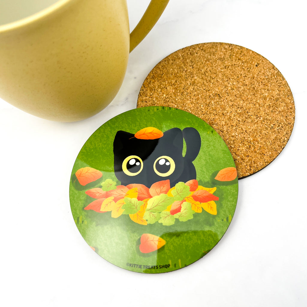 Adorable coaster featuring a black cat playing in a pile of autumn colored leaves